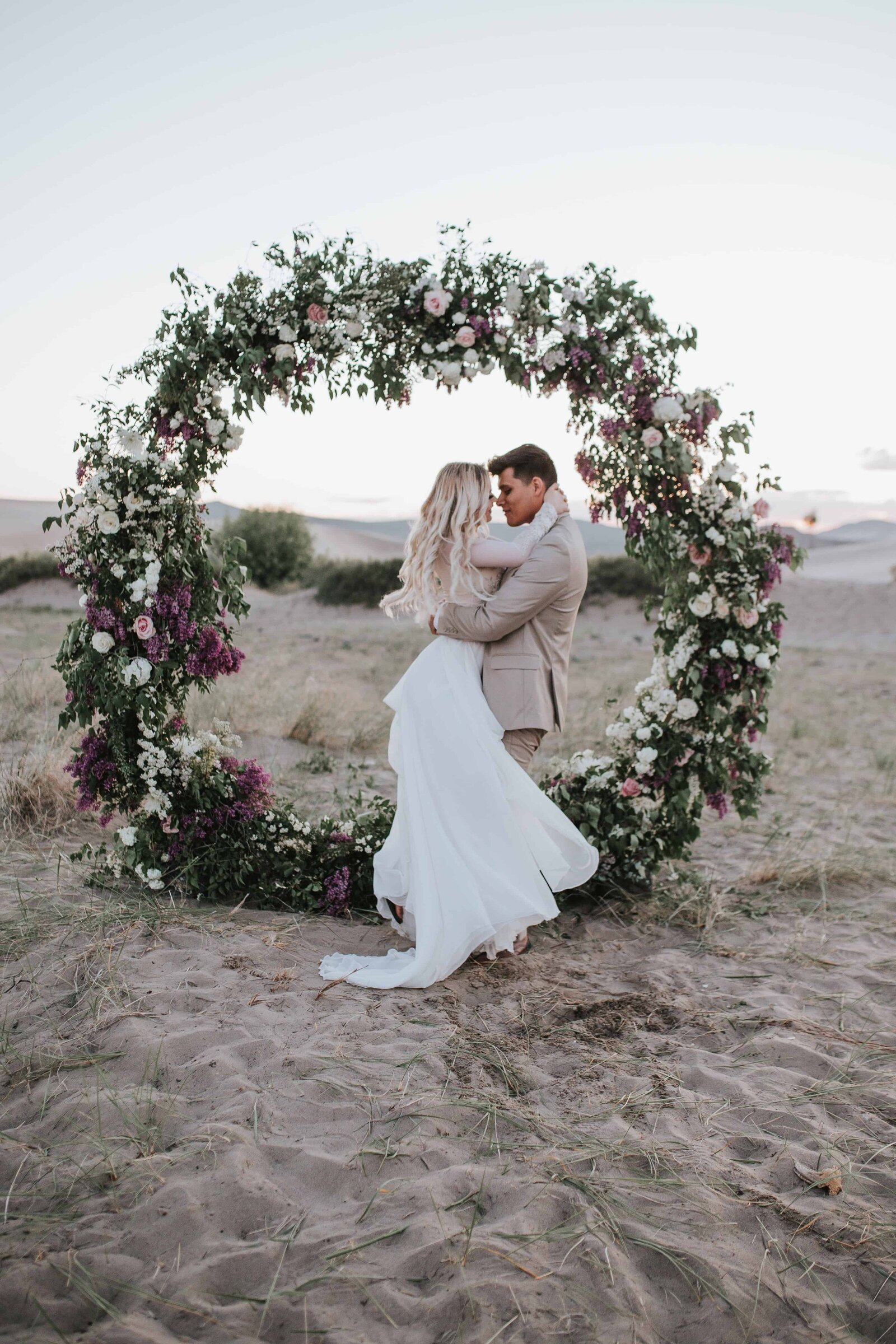 Sacramento Wedding Photographer captures groom lifting bride in front of floral arch