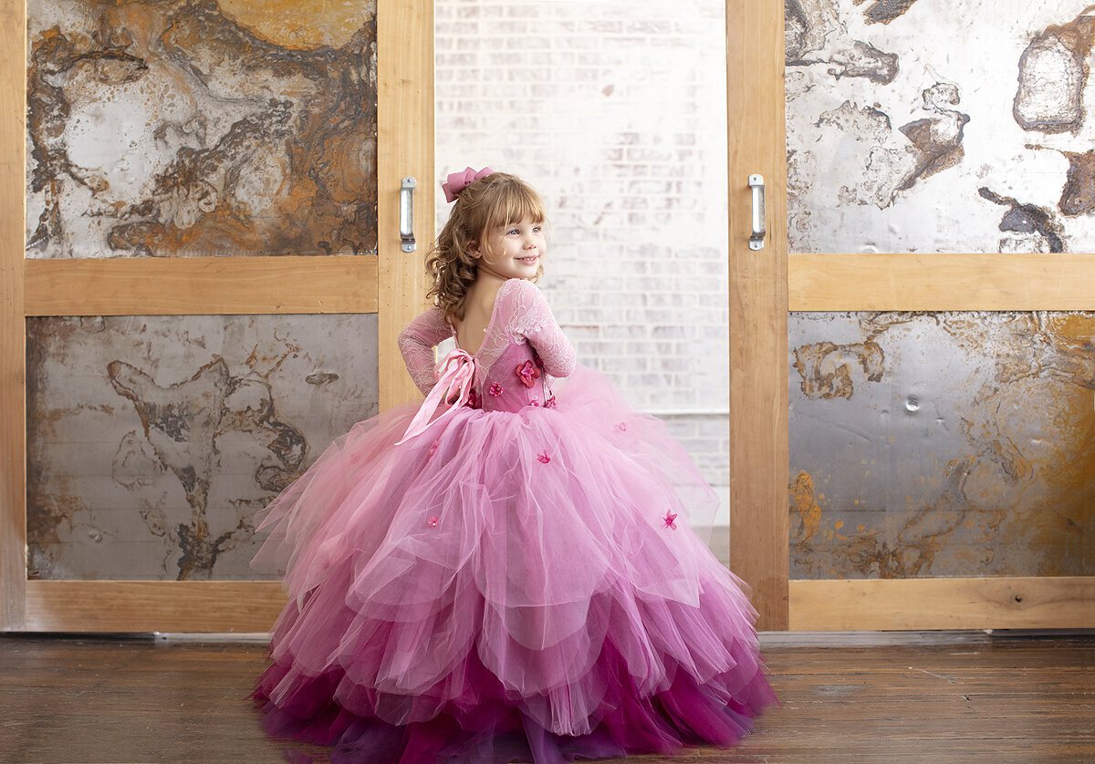 Girl child poses in pretty pink gown at Dallas photography studio.