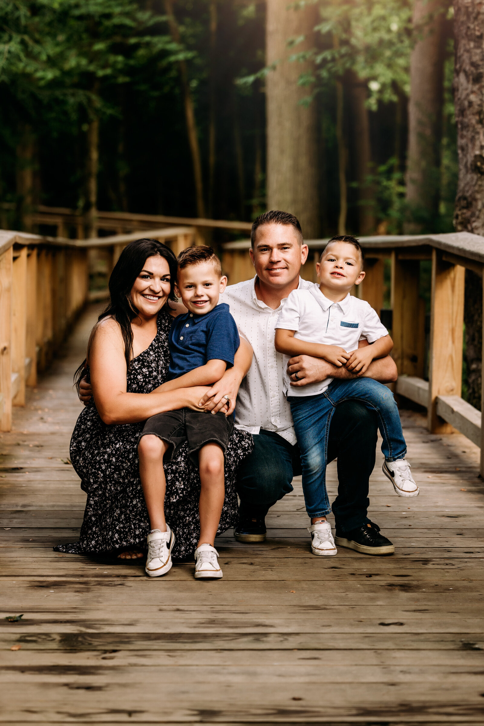 Mother and father snuggle up with their 2 boys along a wooden walkway