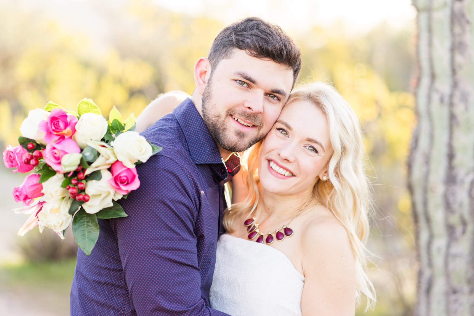 Couple cuddling in front of cactus with pink bouquet