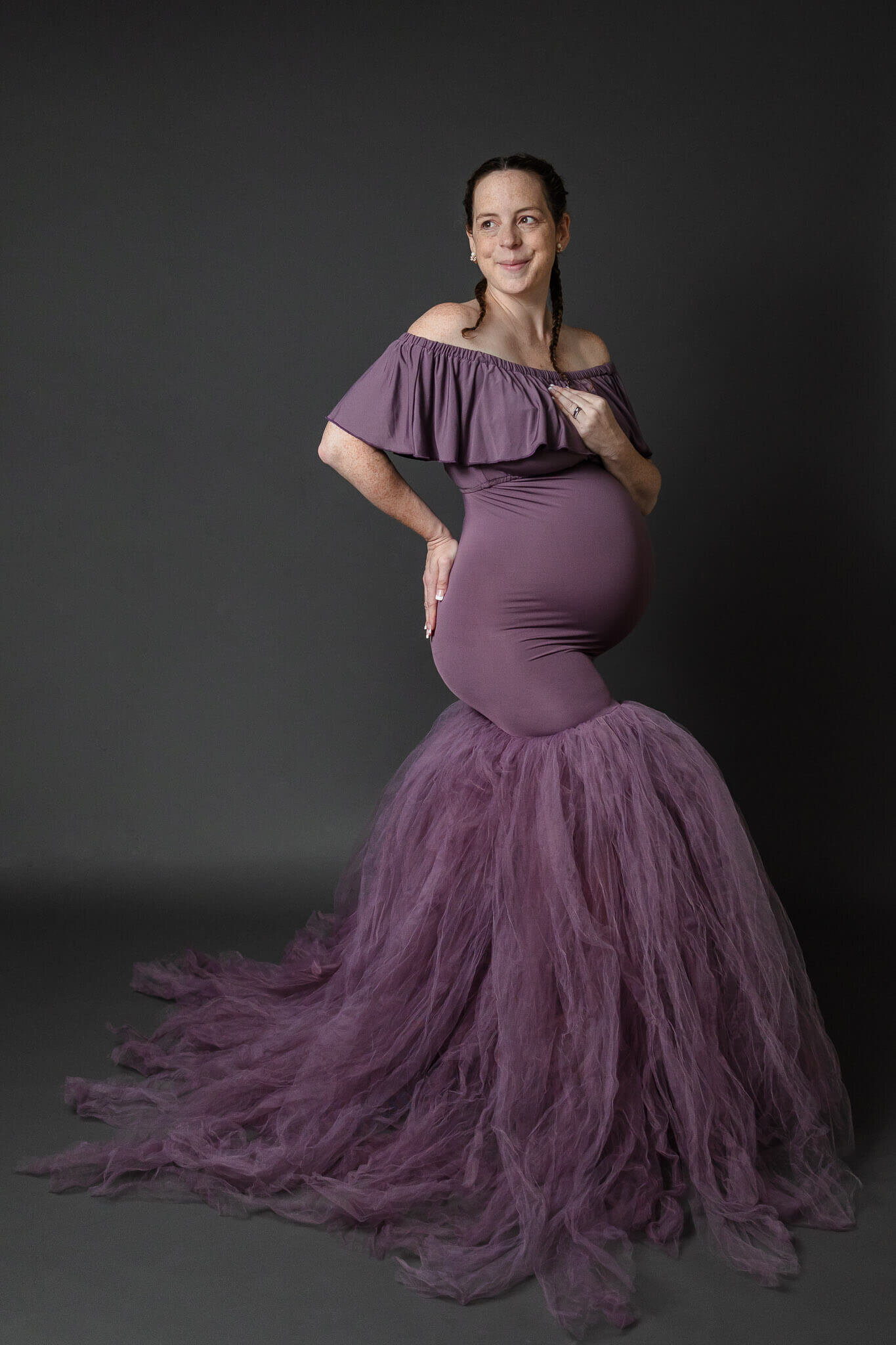 An expecting mother posing in a purple mermaid gown.