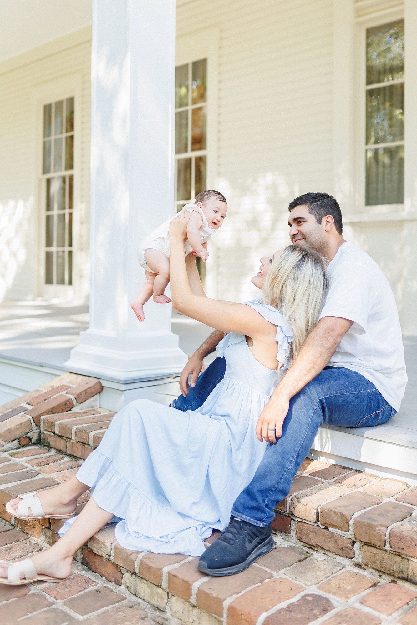 Mother and father sitting on steps smiling at their baby girl during their outdoor family photo session in Grand Forks, North Dakota. 