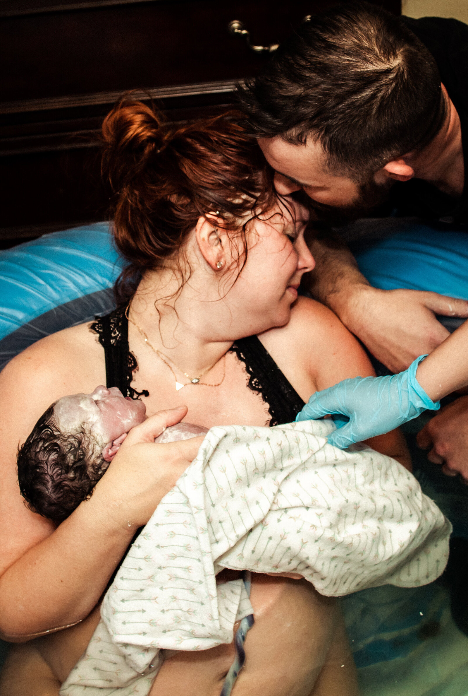 Dad kissing moms forehead and she embraces their new baby in the birth tub