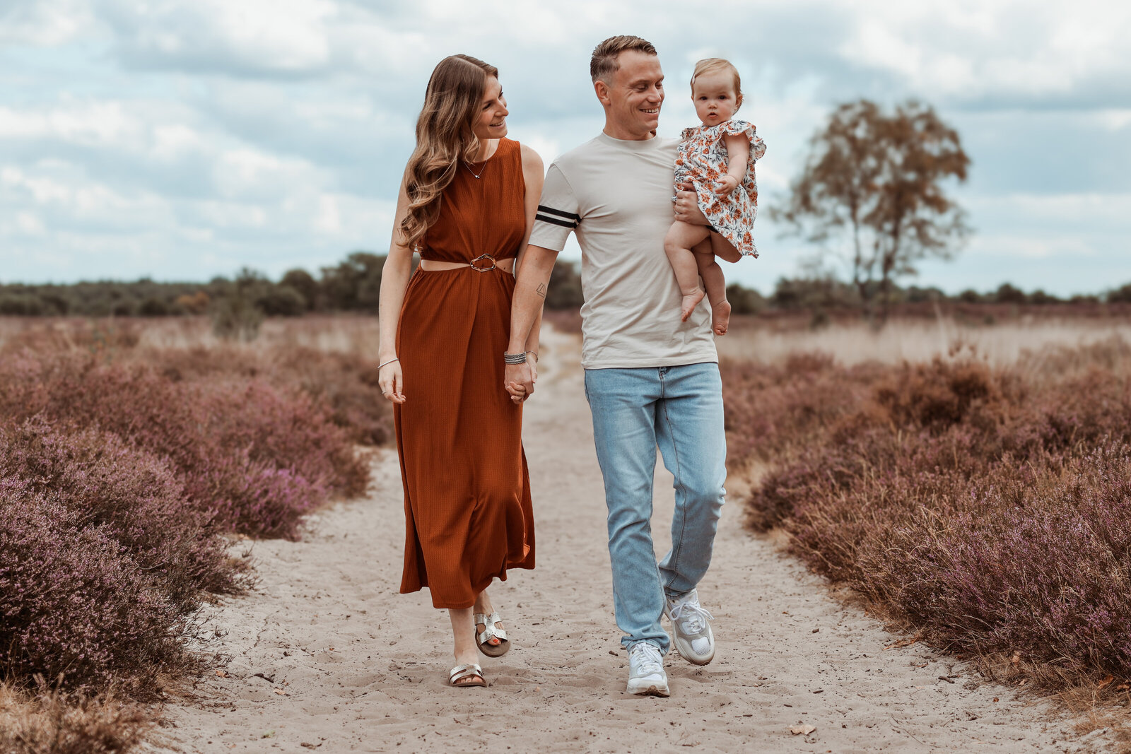 jong gezin lopend op zandpad tussen de bloeiende heide, vader heeft kindje op zijn arm