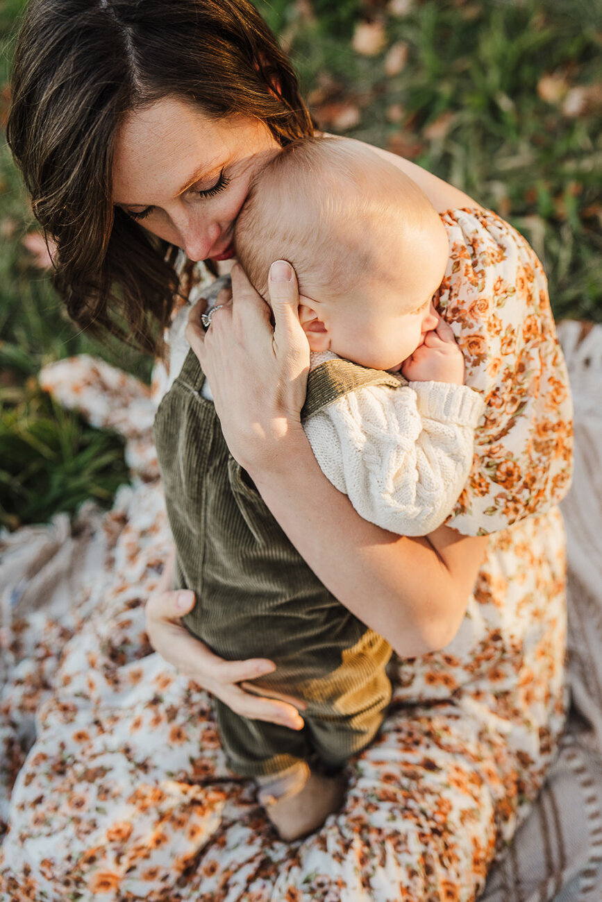 woman holds baby to chest in golden light for boston family photos