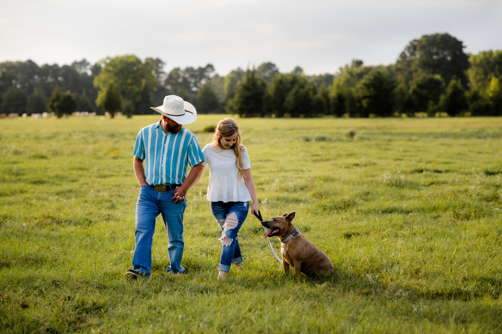 outdoor engagement session in little rock ar with man in a cowboy hat and woman holding hands and playing with their dog