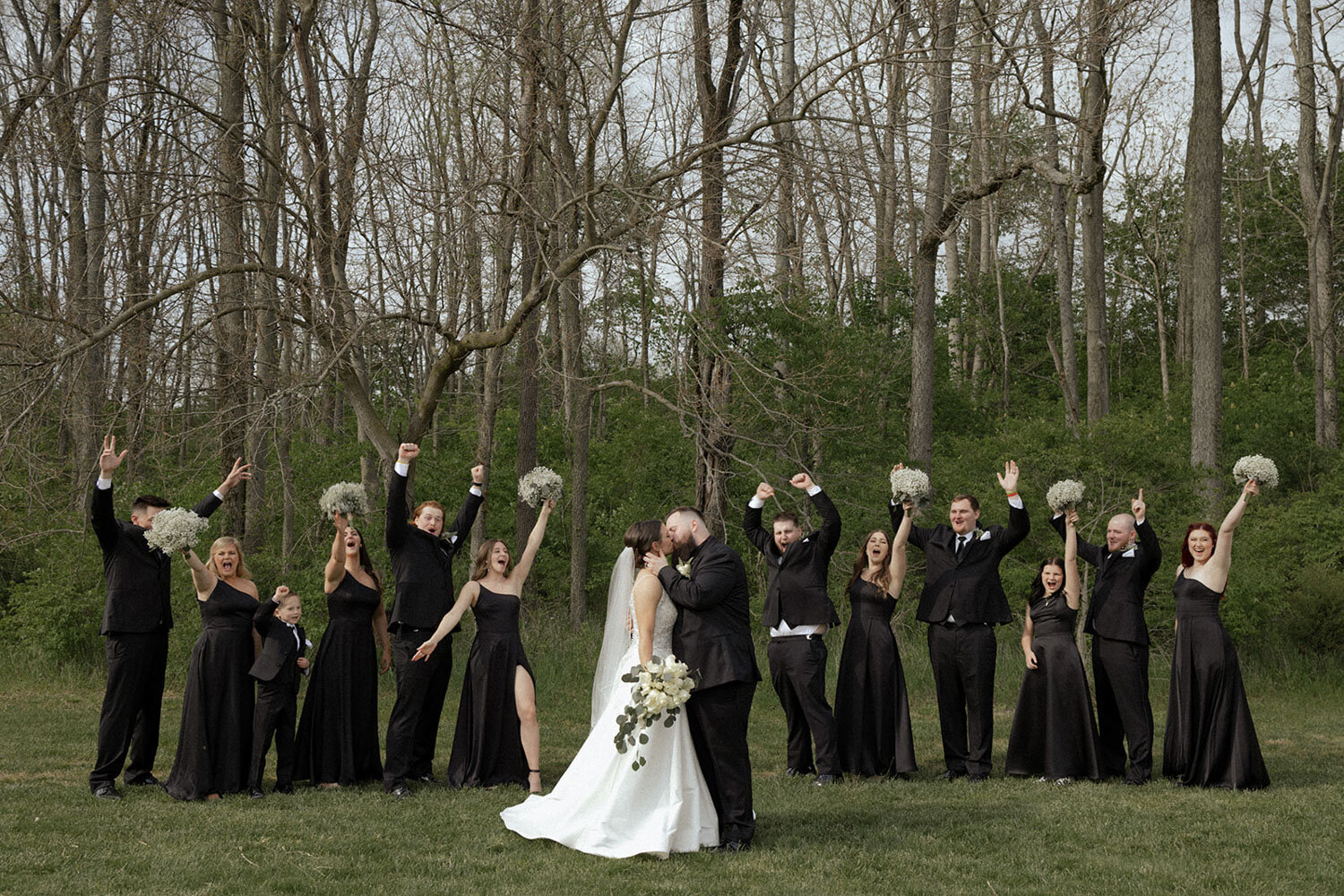 Wedding party cheering as bride and groom kiss in a wooded setting