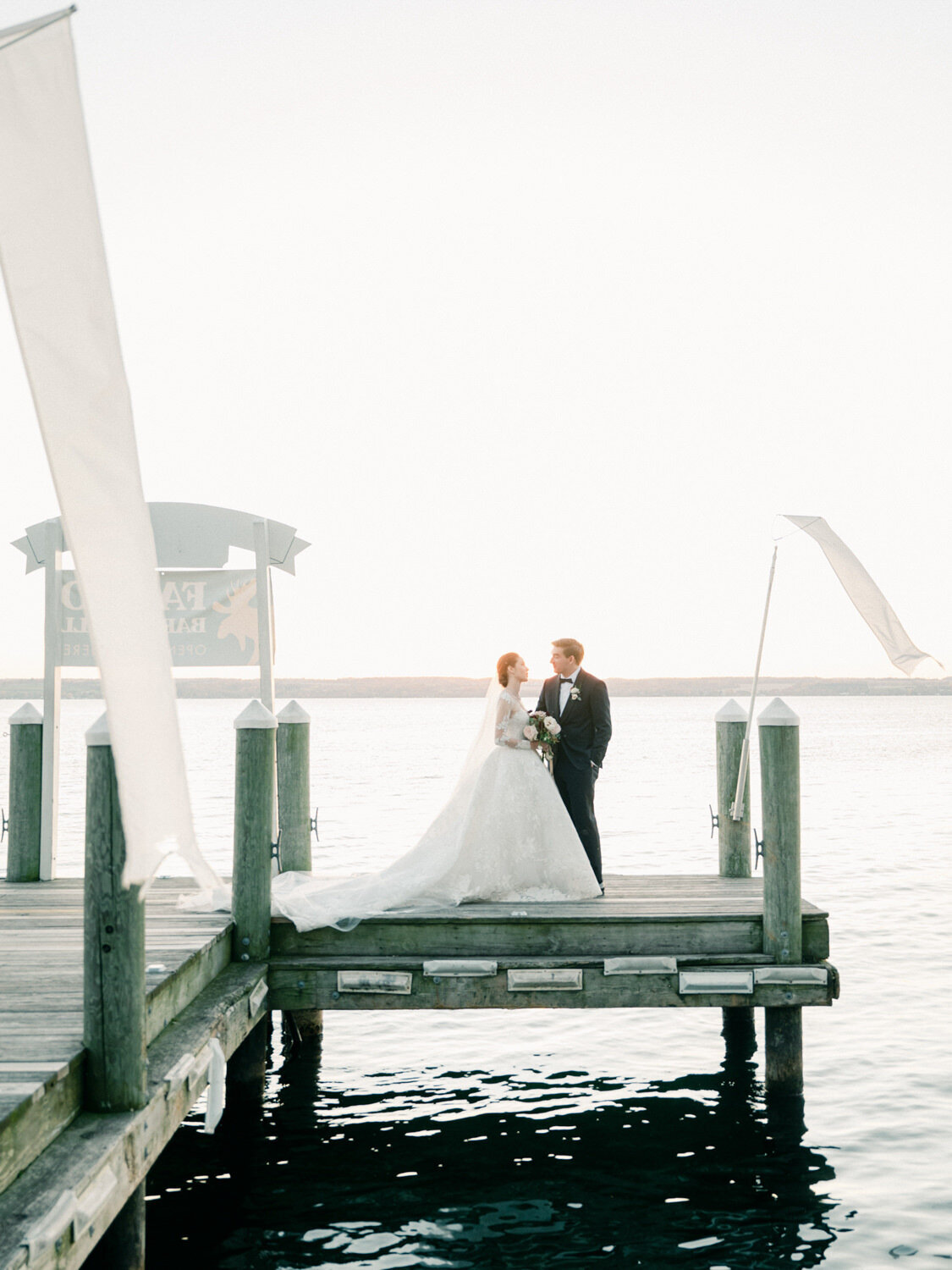 A fall wedding couple pose for the camera on a dock with the Finger Lakes behind them.