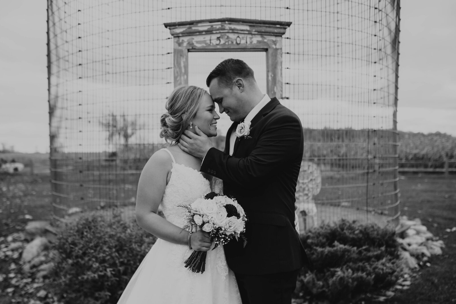 black and white photo of bride and groom looking at each other smiling while she hold her bouquet of flowers