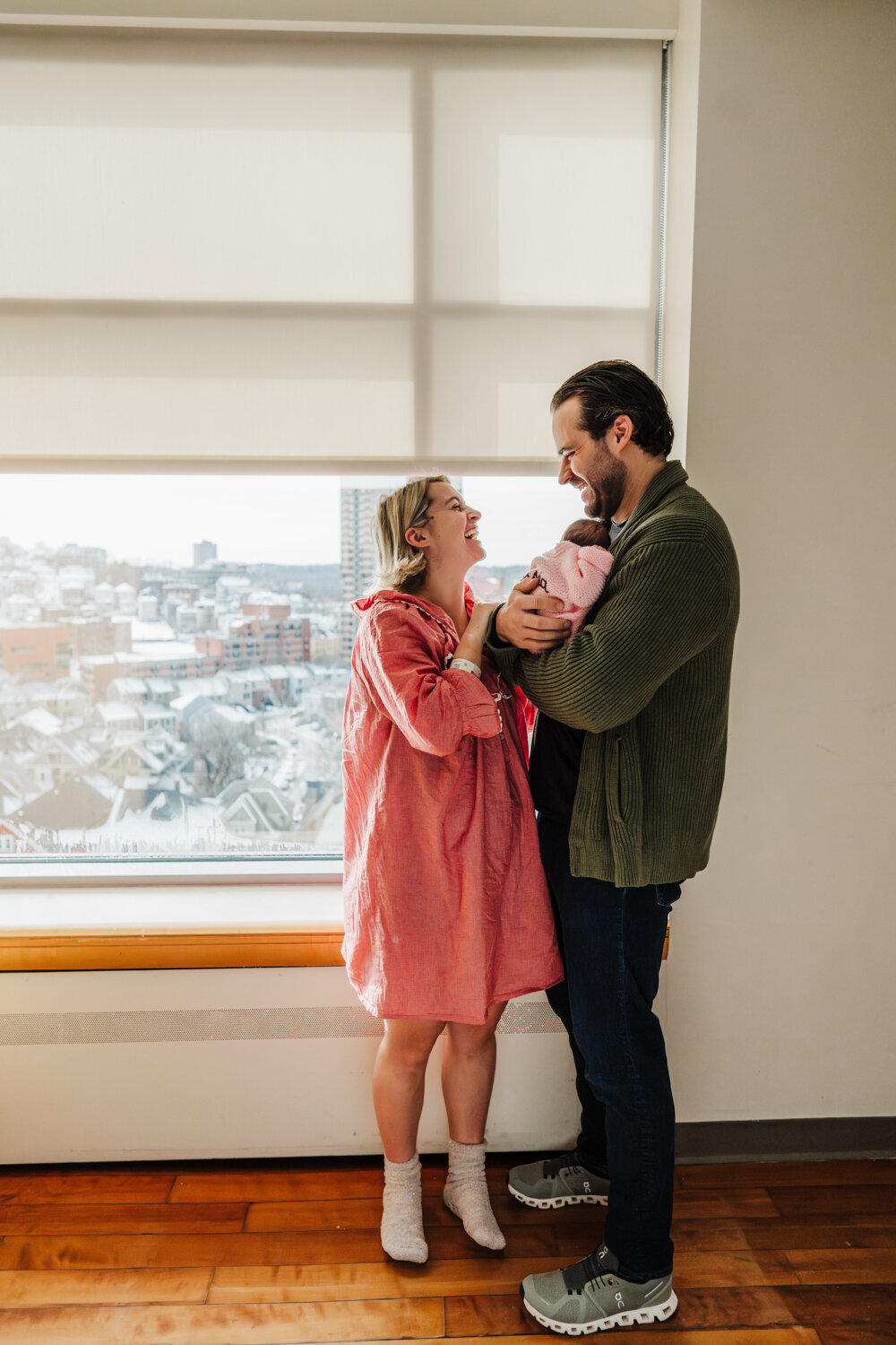 mom and dad stand by hospital window laughing after birth