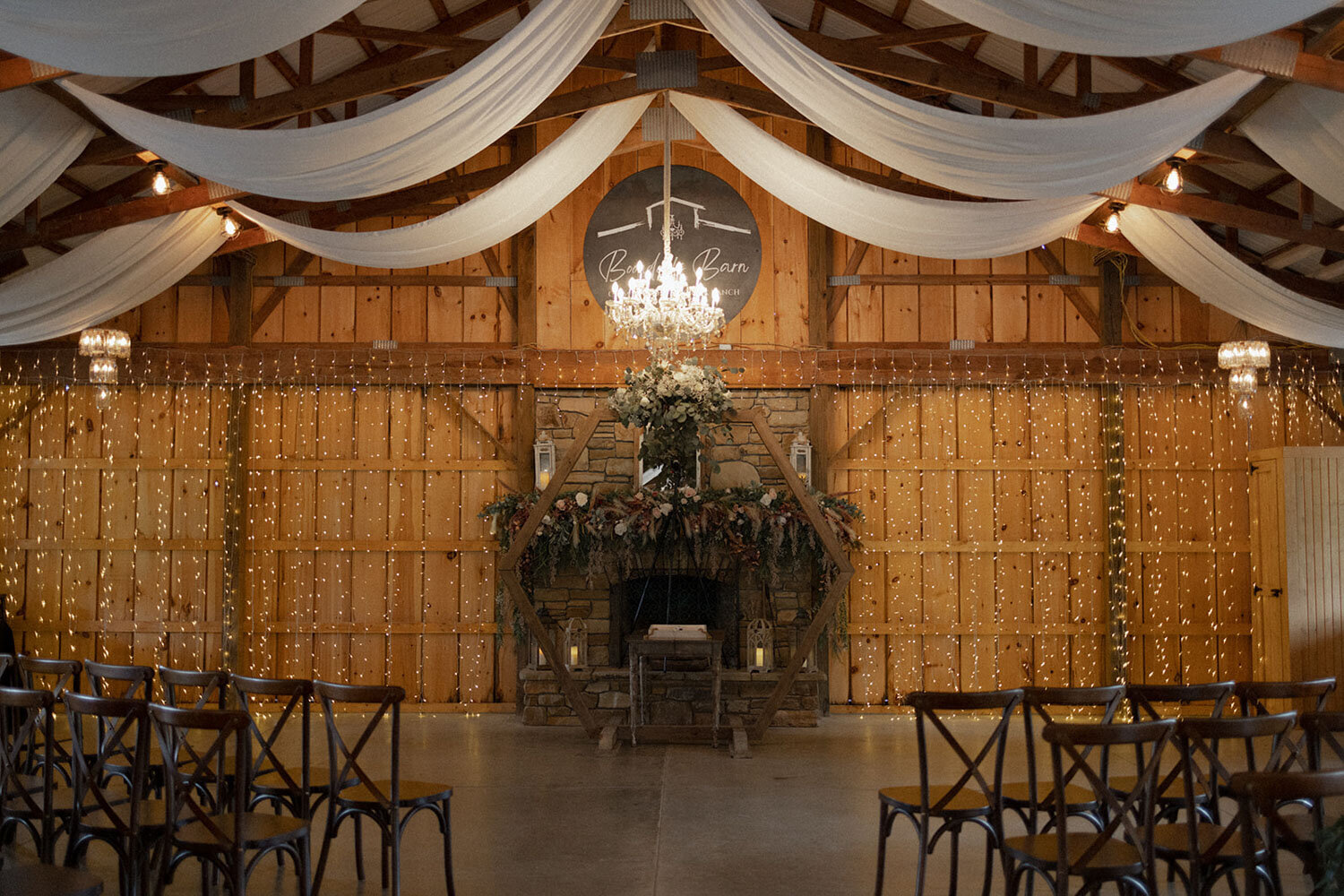 Indoor rustic barn venue decorated with draped fabric and chandeliers