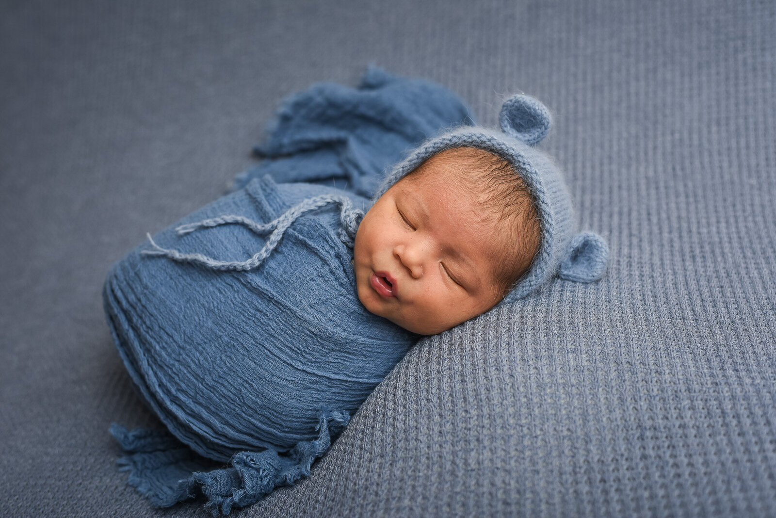 newborn baby laying on his side swaddled in blue  blanket