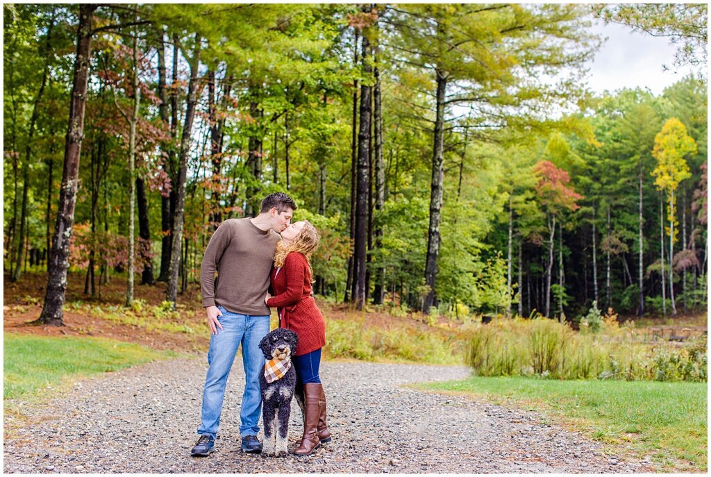 couple kissing with dog and tall trees in the background