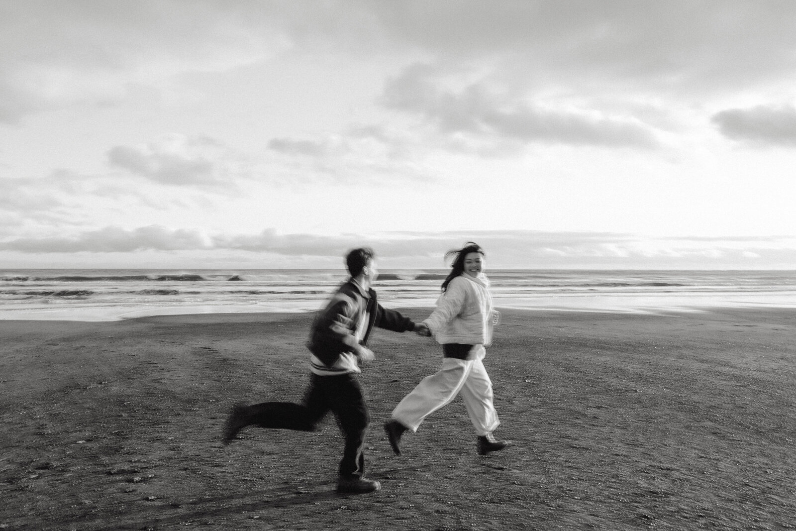 A couple holds hands and runs along the beach at their beach engagement session in Nova Scotia. 