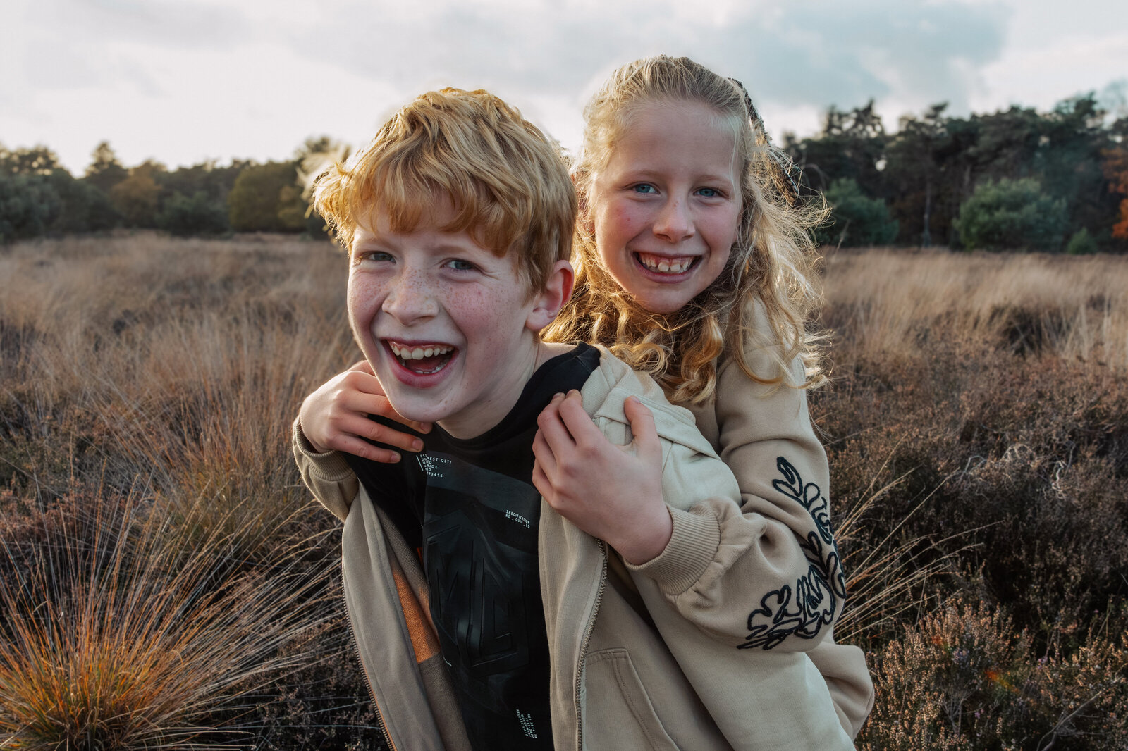 broer met zusje op zijn rug in de heide met zonsondergang