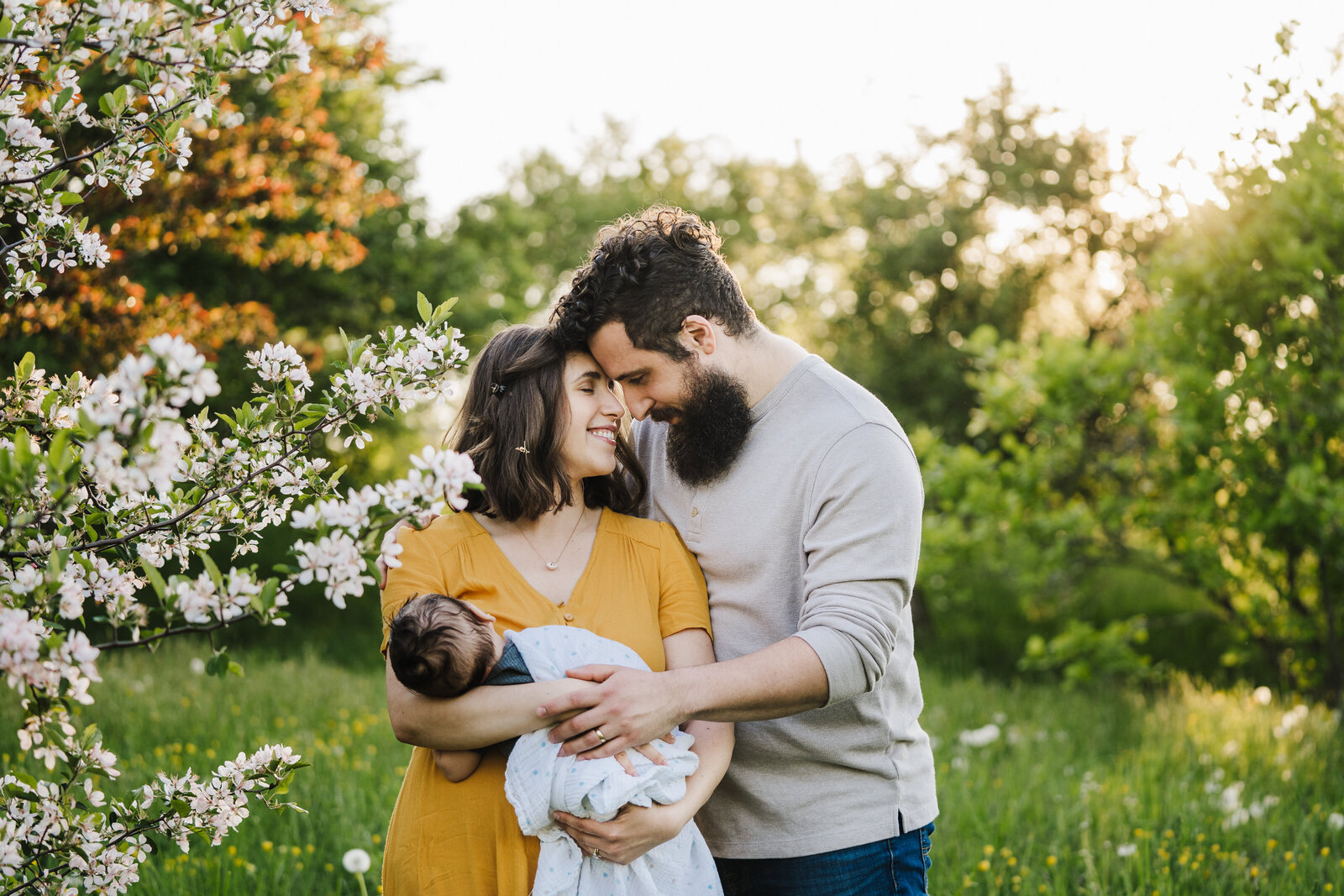 parents of a newborn baby stand in tree blossoms for spring newborn session