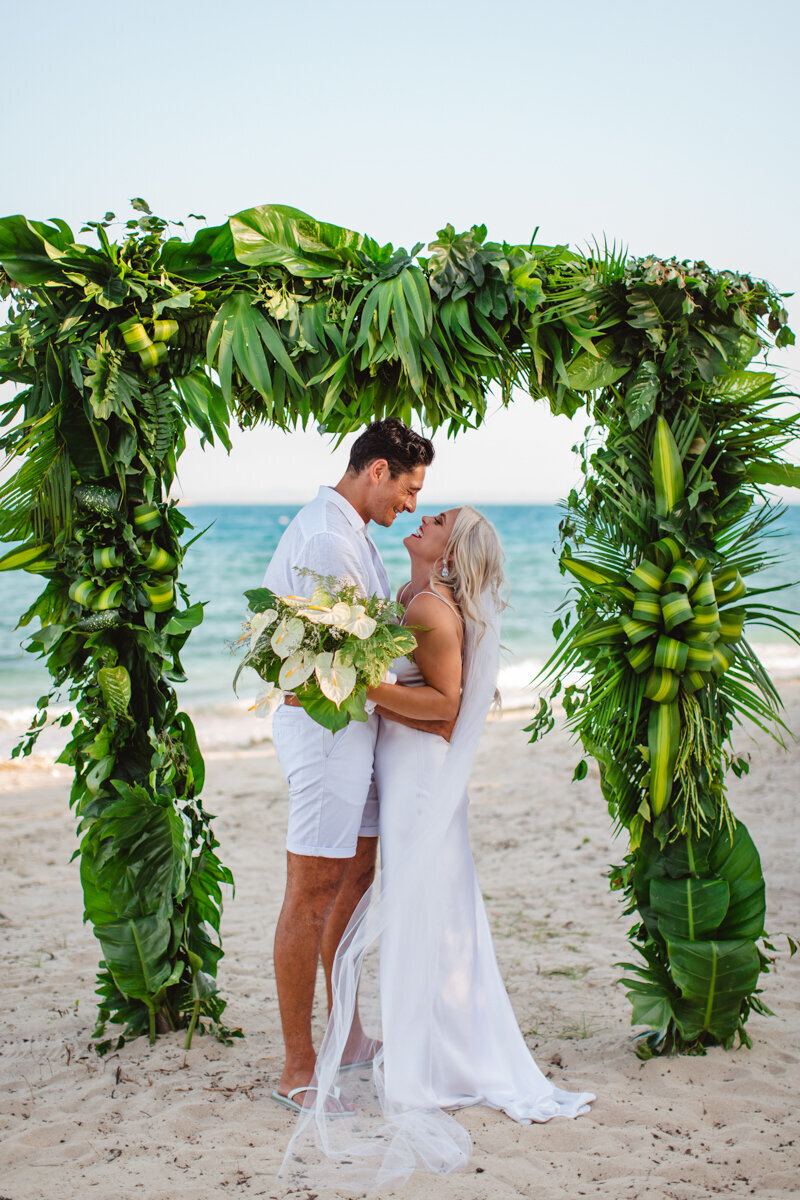 bride and groom under green arch on beach