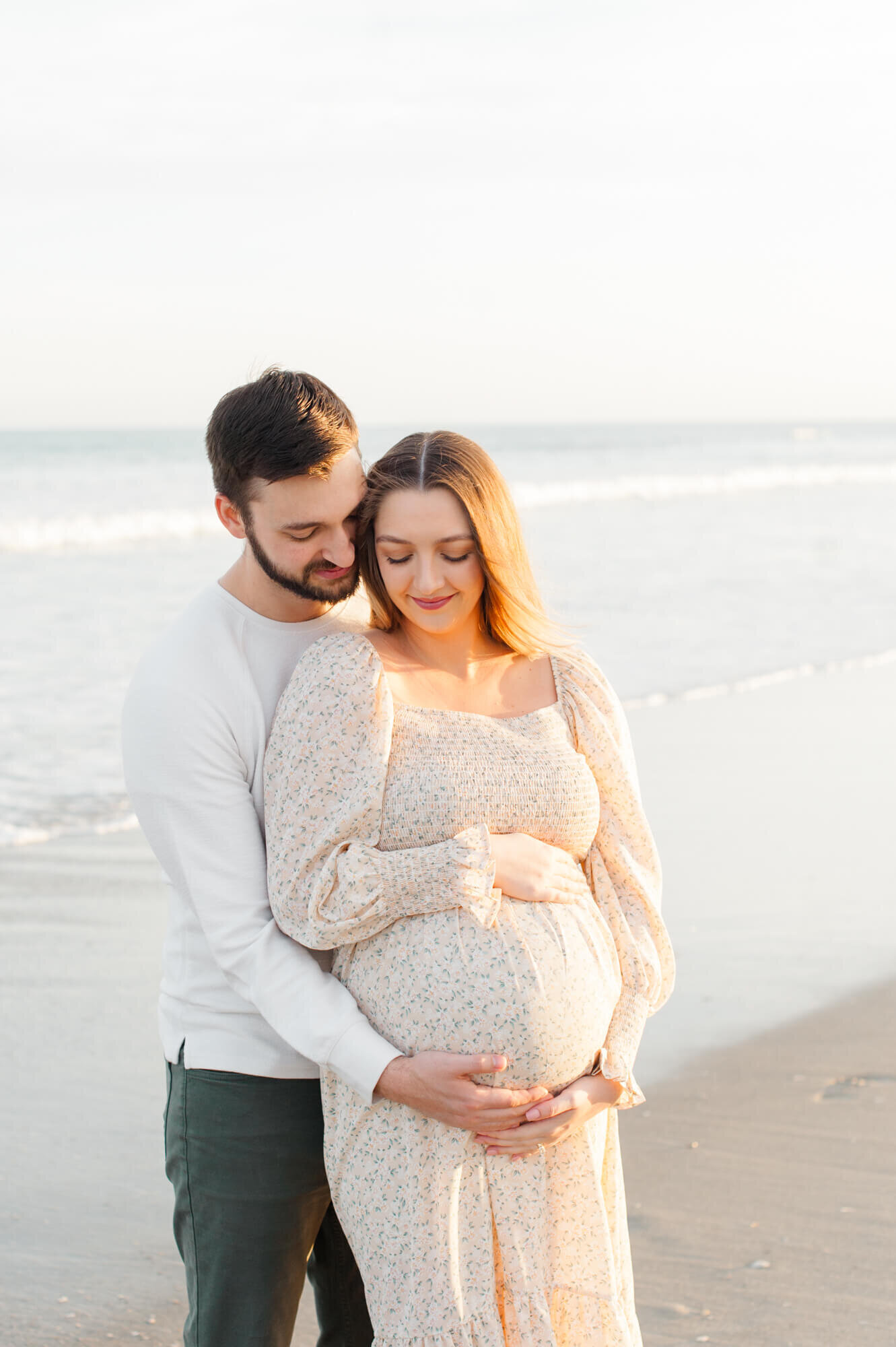 Pregnant couple cuddled close near the shoreline holding moms pregnant belly