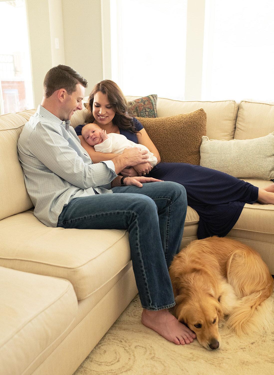Parents and siblings cuddle on the couch with their newborn in a warm, relaxed setting. A lifestyle newborn session by Moments in Light Photography.