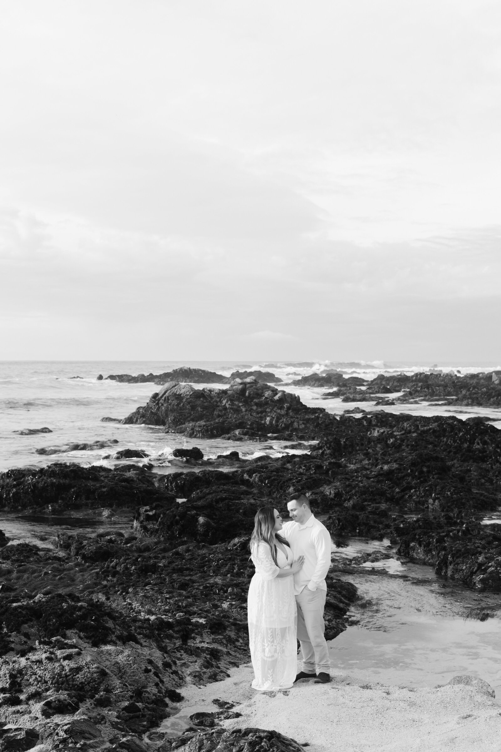 An engaged man and woman take photos on the beach in Pacific Grove, Monterey, California near Big Sur.
