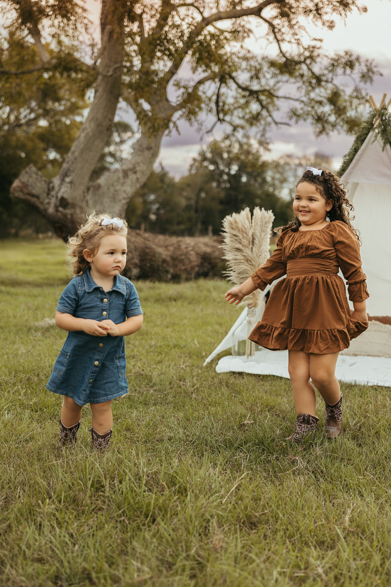 Two young siblings playing together during a family session in a farm field in Aiken SC with a boho teepee setup in the background.
