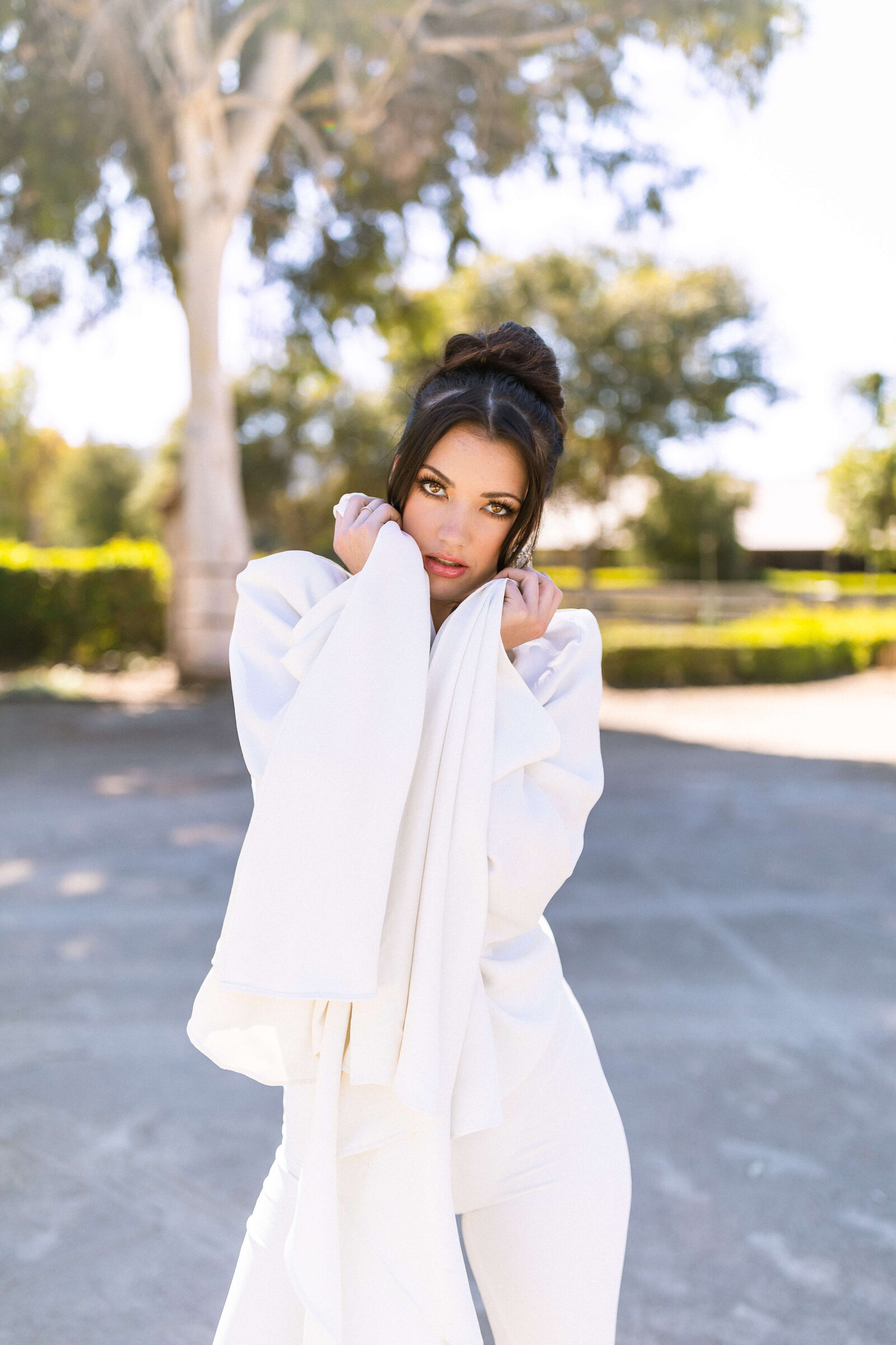 girl with dark hair doing a model pose in an all white outfit in a park