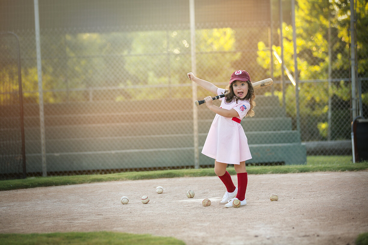 Girl playing with baseball bat during fun child photoshoot.