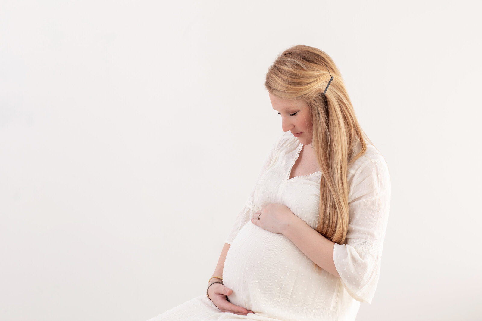 Side profile of an expectant mother in a white fitted gown, gently cradling her belly—styled and shot by Philadelphia maternity photographers