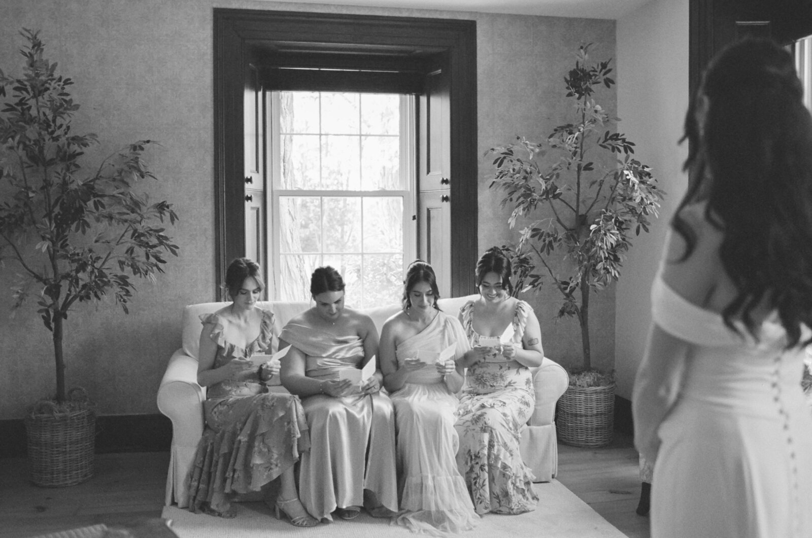 Black and white image or bridesmaids opening letters from the bride on a couch