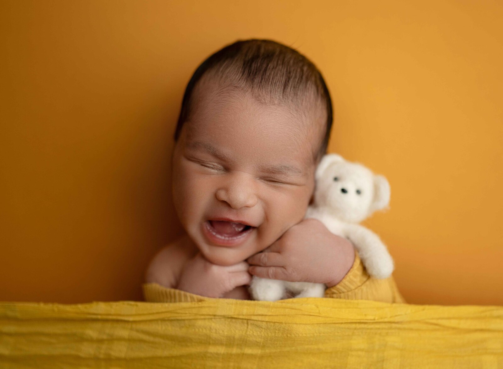 Baby holding a teddy bear and smiling in his sleep.
