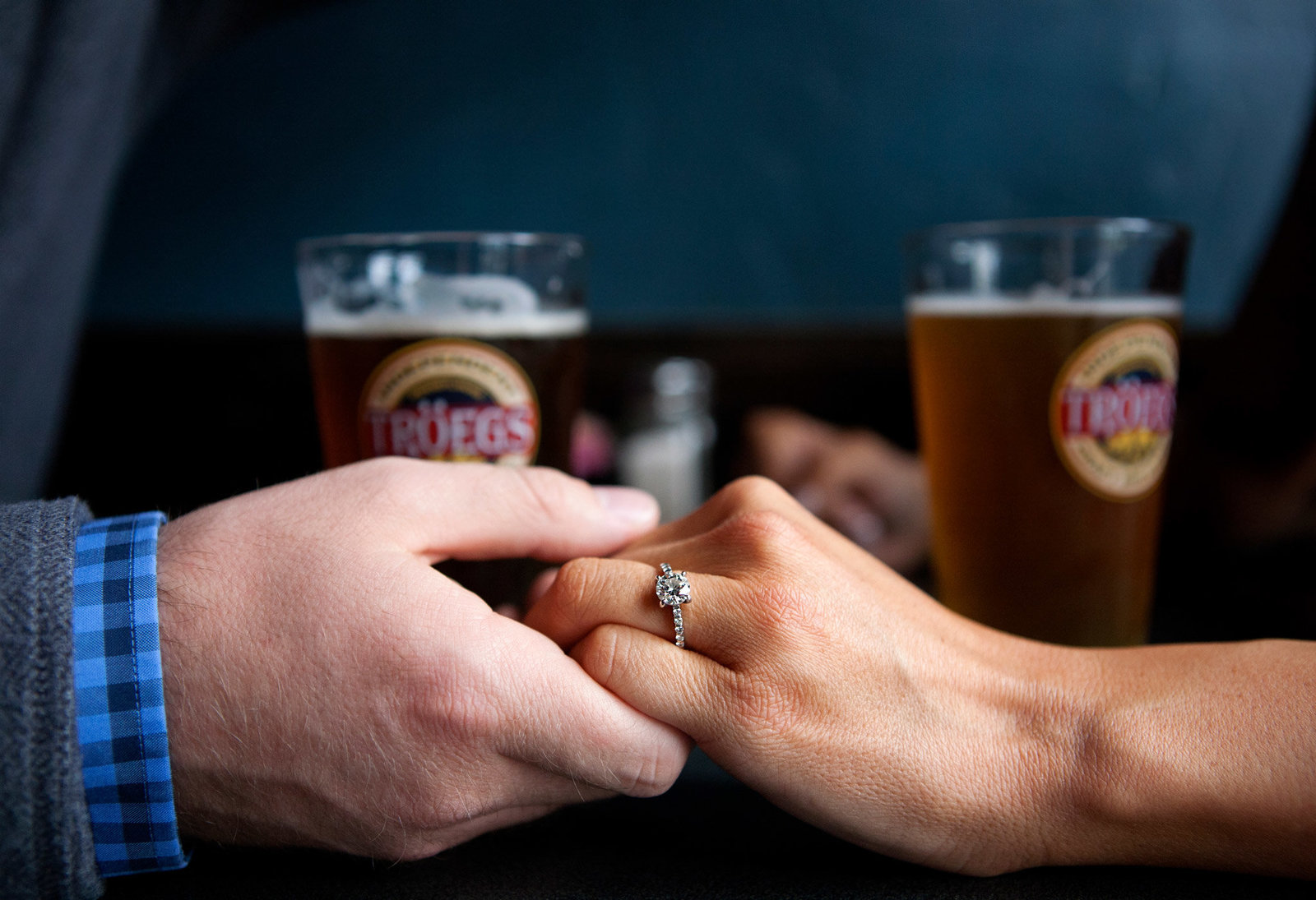 Engaged couple holding hands on table with beer