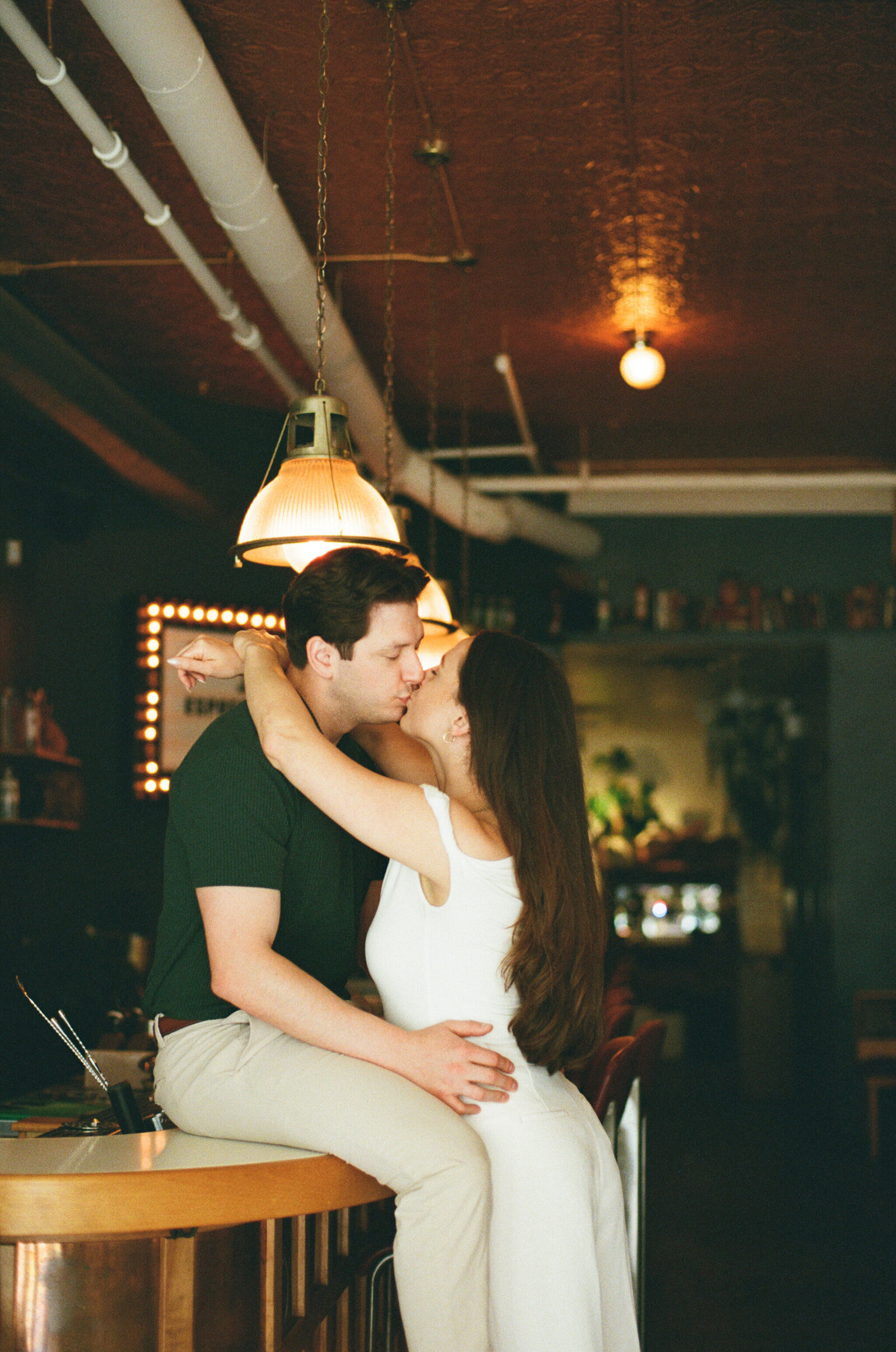 A man sits on a bar at a local restaurant in Halifax while his fiance leans over to kiss him.