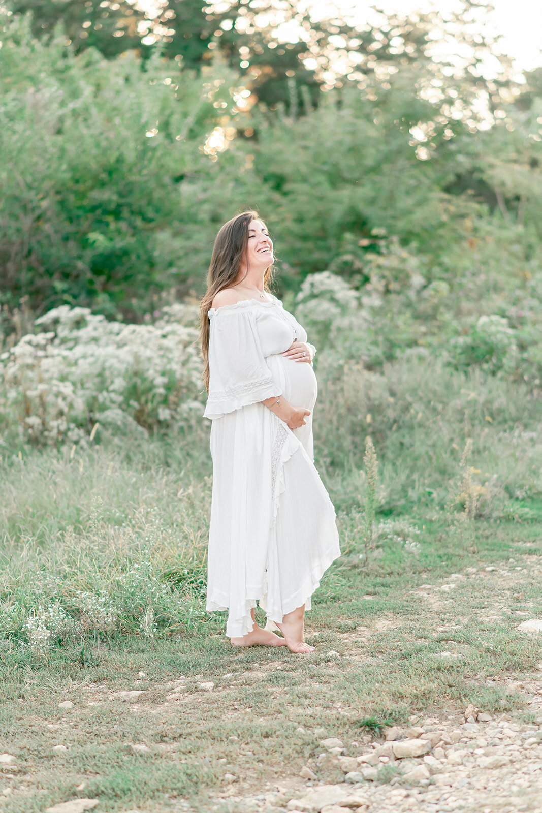 pregnant woman in white dresses stands in field of wildflowers by Nashville maternity photographer Kristie Lloyd