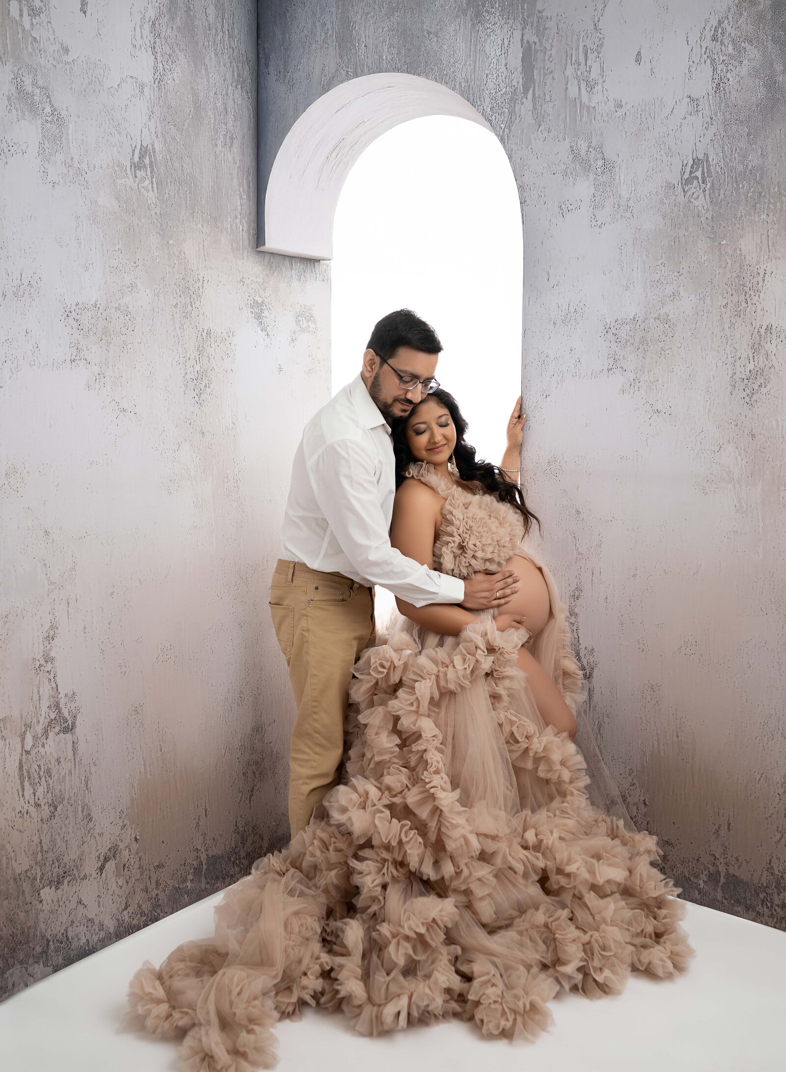 Arch panels with couple posing in front of them. They are cuddling and look at baby bump. Photo taken at Atlanta Photo Studio.