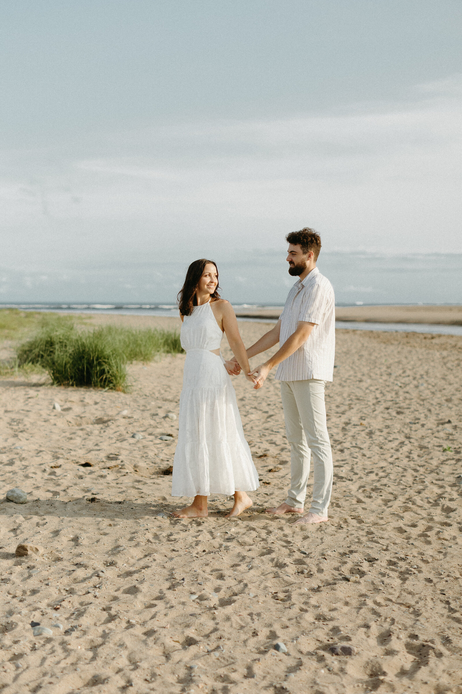 A couple holding hands walking on the beach in Lawrencetown during their engagement session.