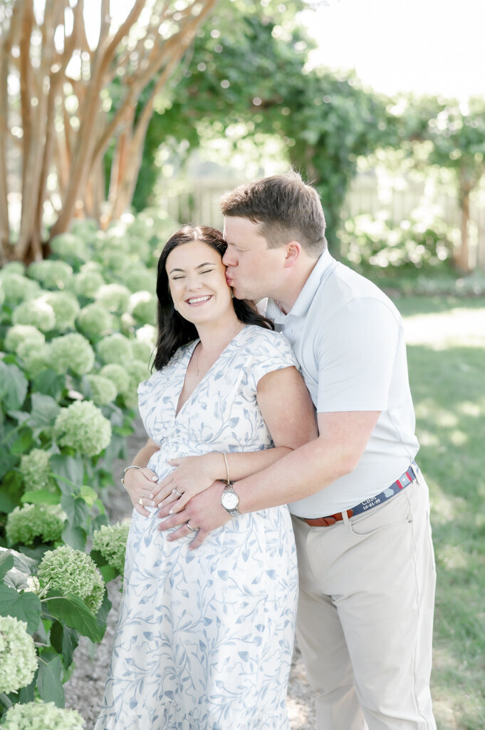 Pregnant couple hugs standing beside white flowers