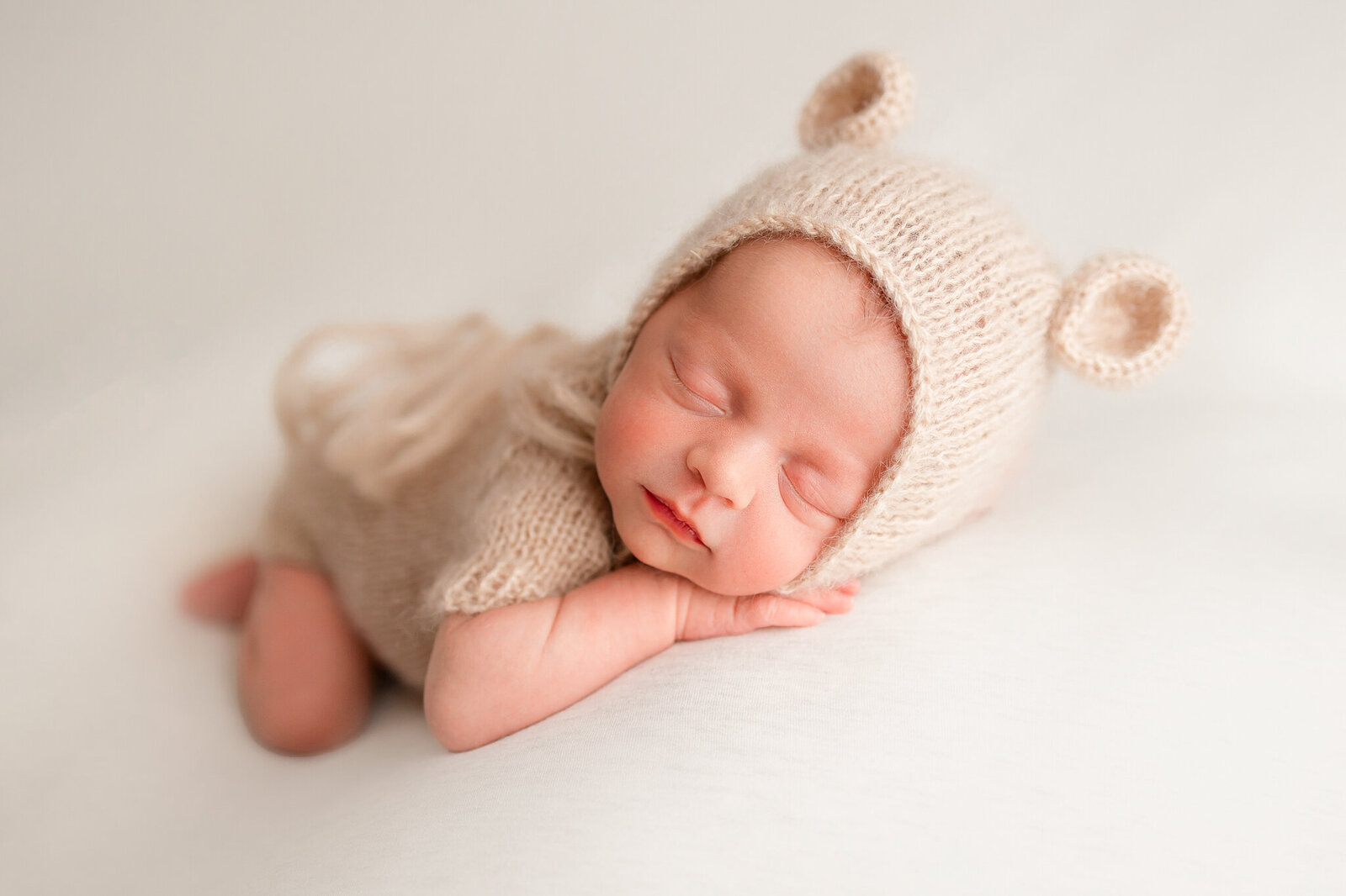Beautiful newborn baby boy wearing a soft bear outfit posing with hands on chin