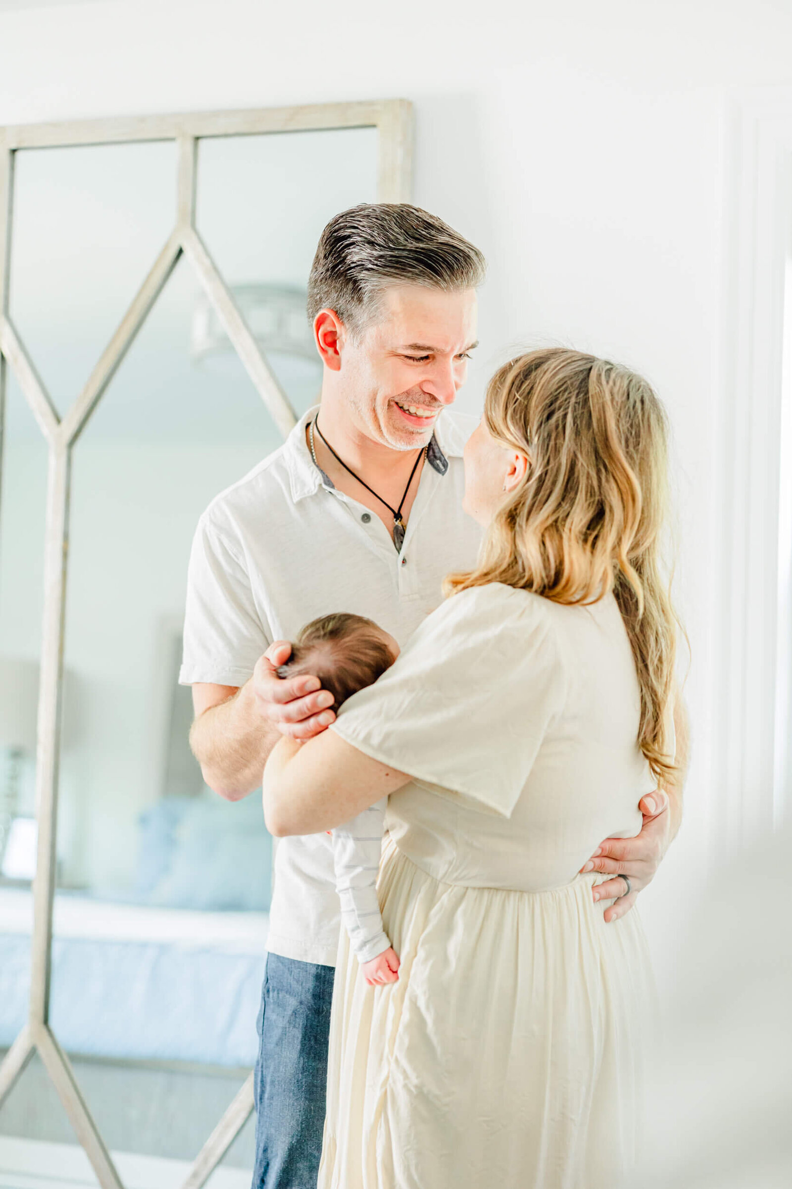 Mom and dad standing and smiling at each other while holding their newborn