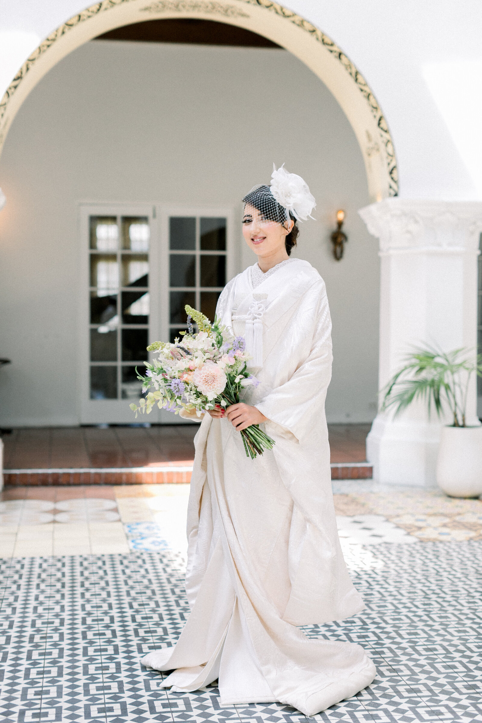 Bride smiling and holding a bouquet in a white shiromuku wedding kimono at The Ebell Club Long Beach in Los Angeles, California. Available for wedding kimono rental in Los Angeles | 白無垢姿でブーケを持つ笑顔の花嫁。ロサンゼルス・カリフォルニアのエベルクラブにて。着物レンタル可能。