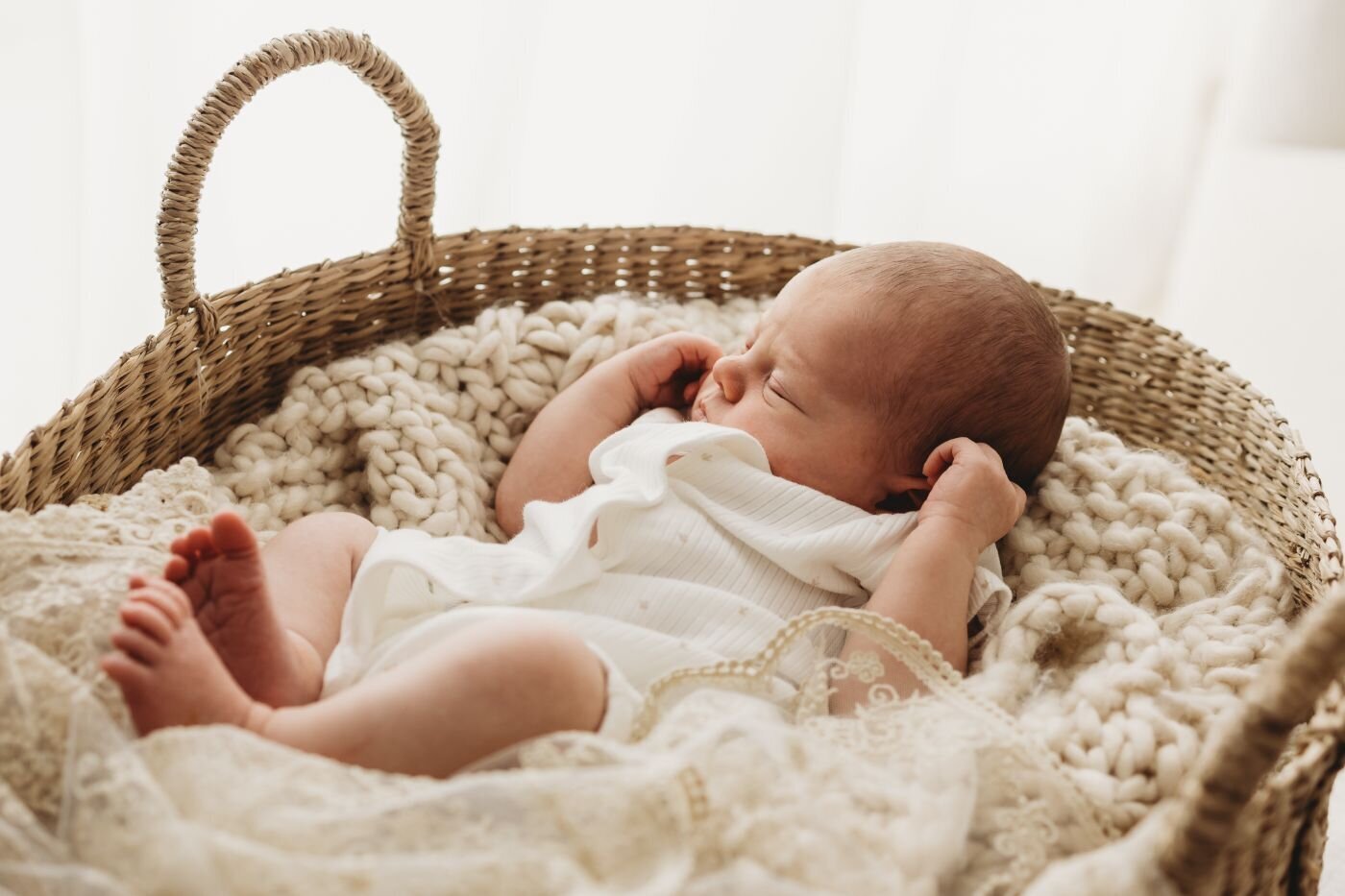 Peacefully sleeping newborn baby girl nestled in a woven basket with soft, textured blankets and a delicate white outfit