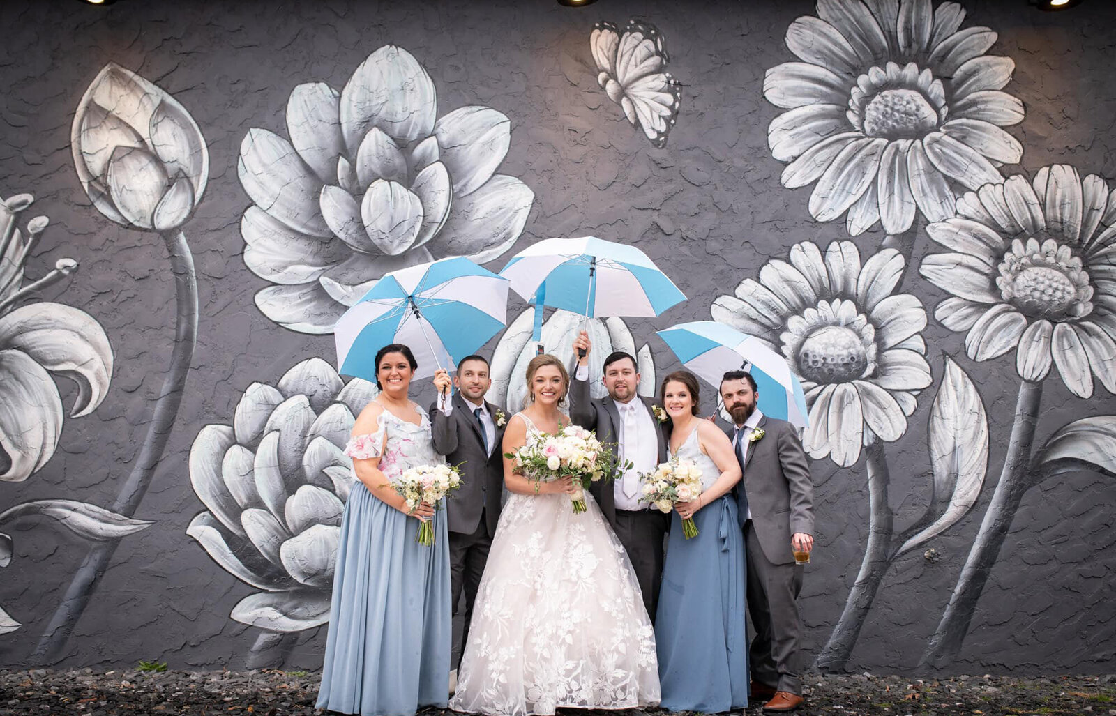 bridal party with umbrellas stand by black and white floral mural wall