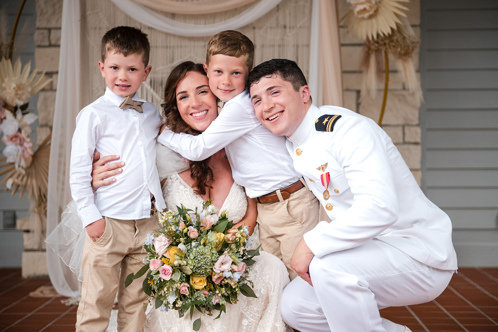 A joyful family moment as the bride and groom pose with two children after their wedding ceremony, captured by CMH Studios during a military wedding in San Antonio.