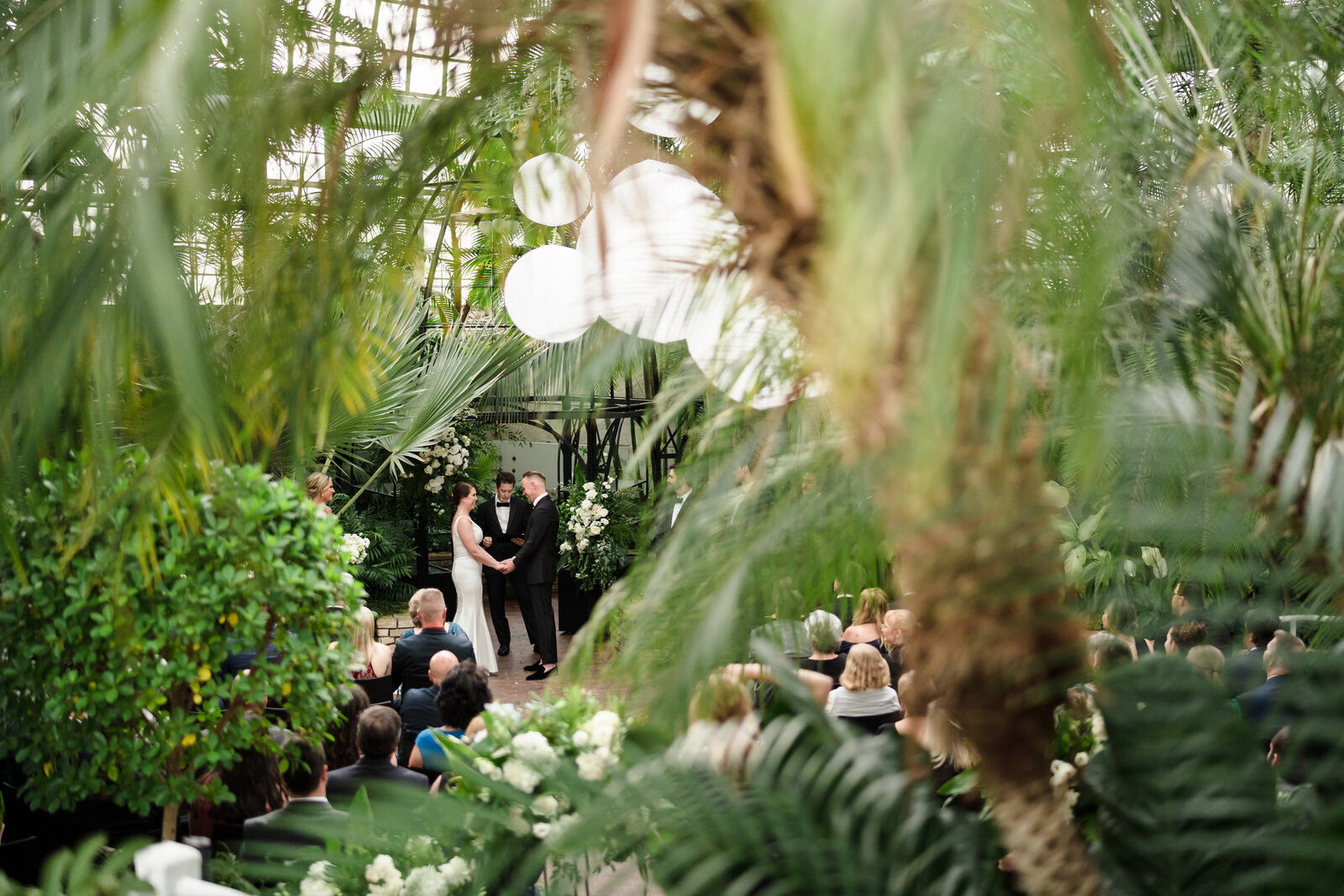 A bride a groom stand at the altar inside the Palm House surrounded by greenery