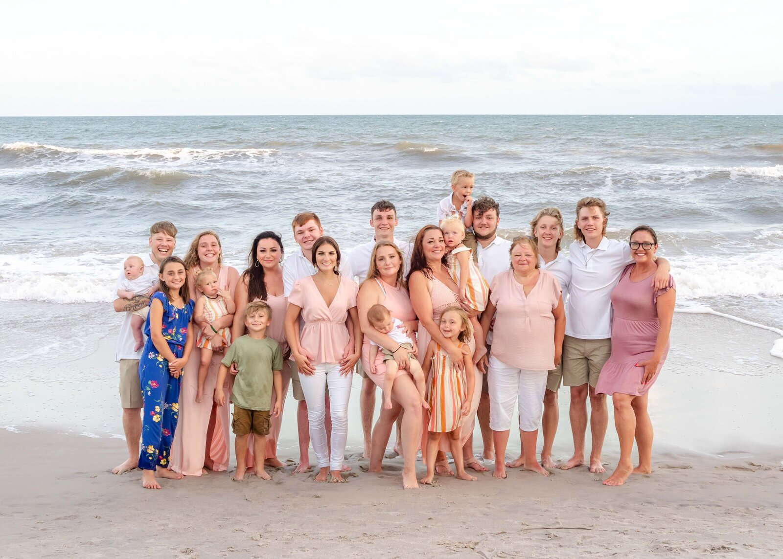 A big family poses on the sands of Ocean Isle Beach, dressed in a mix of pastels and neutrals. The ocean waves add a lively touch, capturing the warmth and connection of a multi-generational reunion. Perfect for artistic family photography in Wilmington, NC.