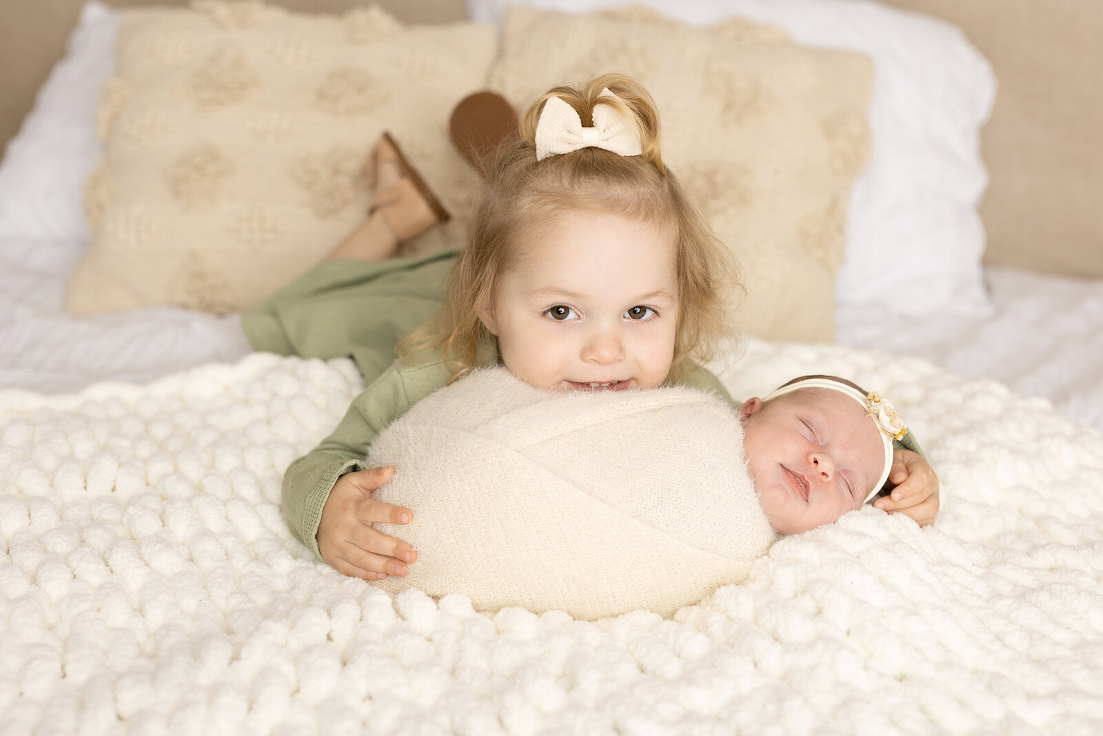 sisters for newborn session laying on bed together