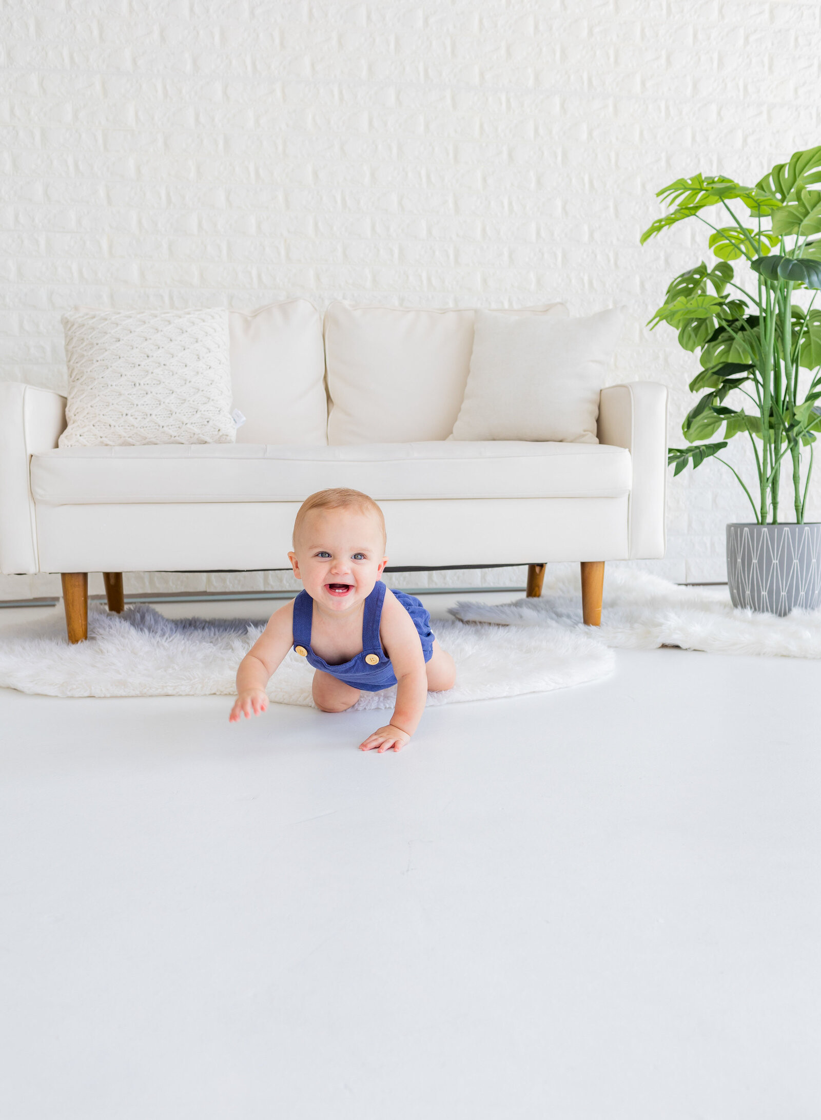 one year old boy smiling in front of couch