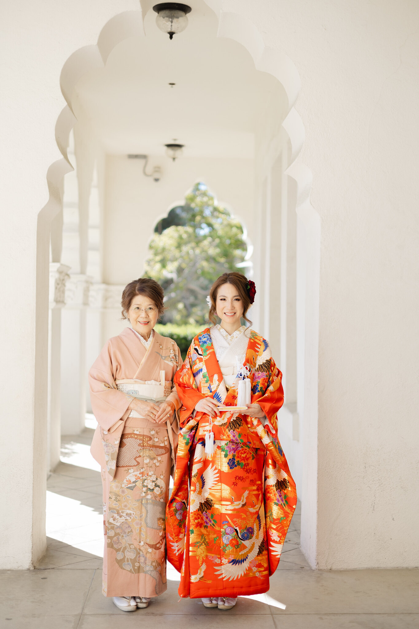 Bride in red iro uchikake kimono standing with mother in pastel kimono at Brand Park Glendale, Los Angeles California. Elegant wedding kimono rental | 色打掛姿の花嫁と淡色をまとう母、ブランドパーク・グレンデールで。ロサンゼルス カリフォルニアのウェディング着物レンタル。