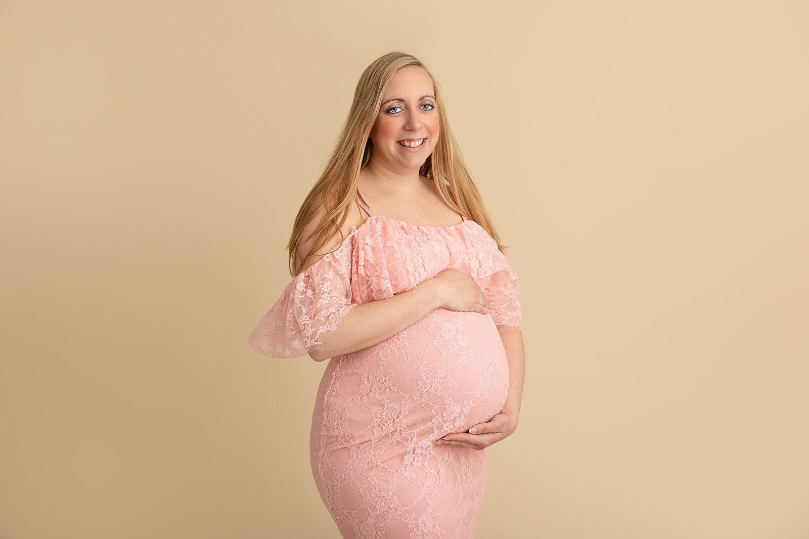 pregnant mom in pink dress posing in studio with baby belly by PHILADELPHIA MATERNITY PHOTOGRAPHER