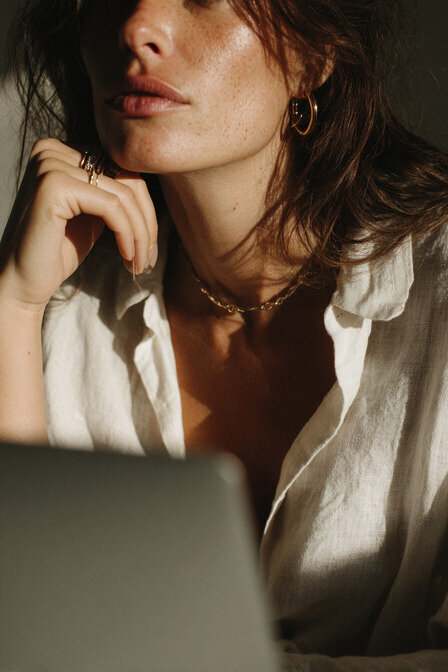 Close-up editorial image of a designer in a linen shirt and gold jewelry working on a laptop, capturing the organic, sophisticated tone of Kathalyst Design Studio.