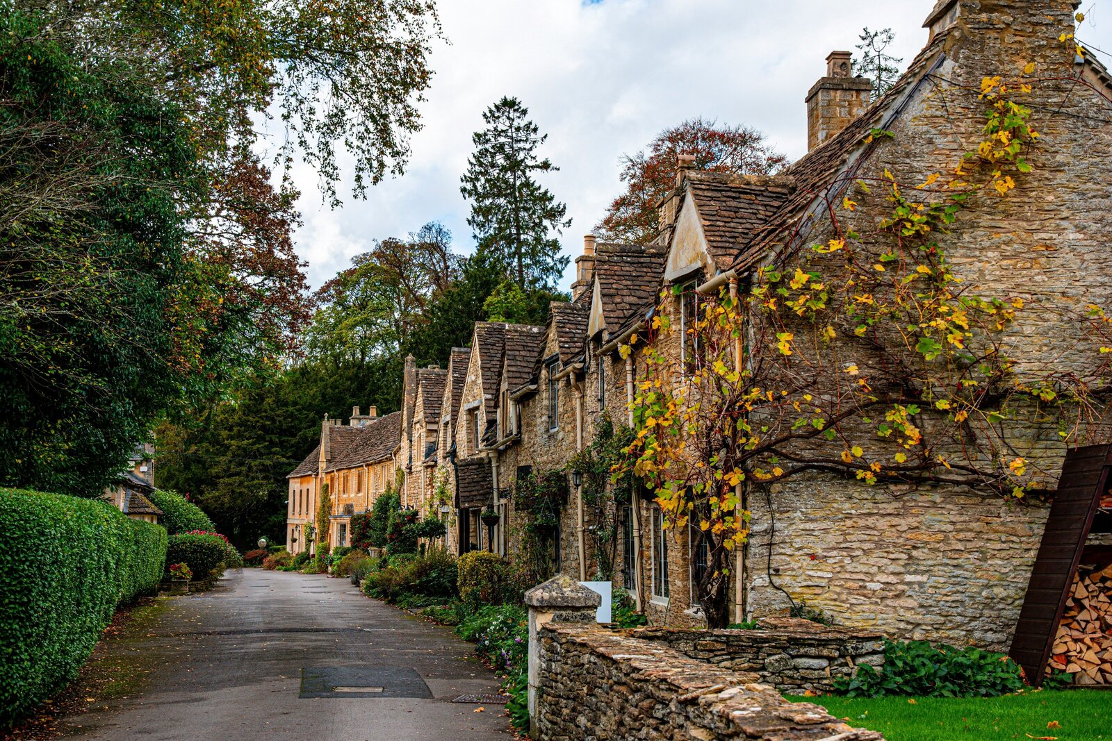 A row of stone cottages lining a street in a Cotswold village surrounded by fall foliage 
